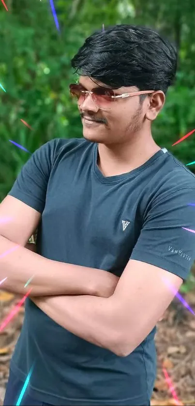 Man in dark t-shirt standing confidently in lush green surroundings.