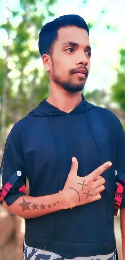 Man in hoodie posing outdoors with a blurred nature background.