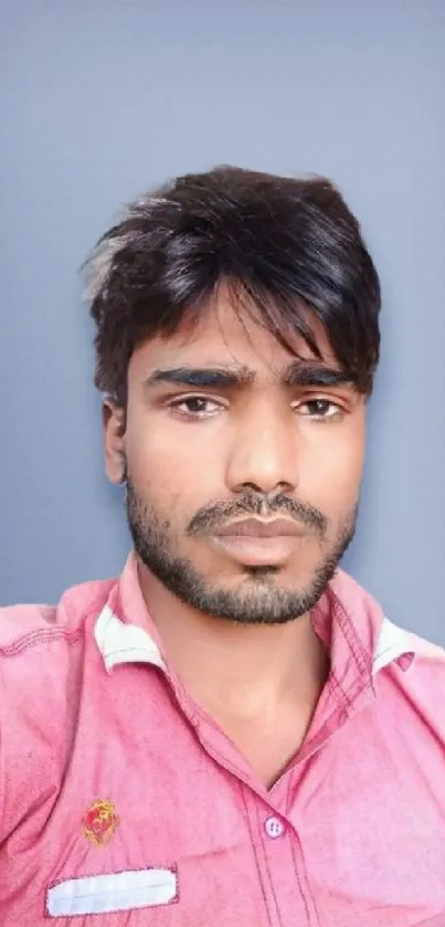 Portrait of a young man in a pink shirt on a blue-gray background.