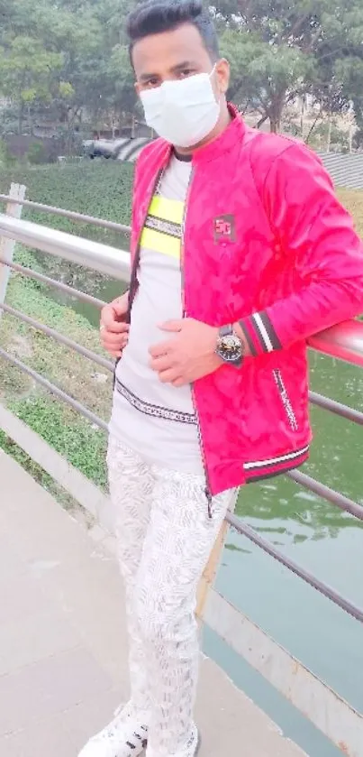 Man posing in red jacket and face mask on urban bridge.