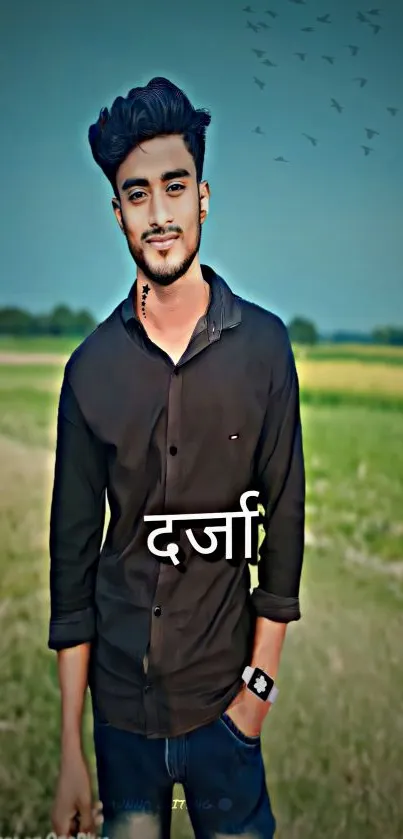 Young man in black attire posing in a green scenic field.