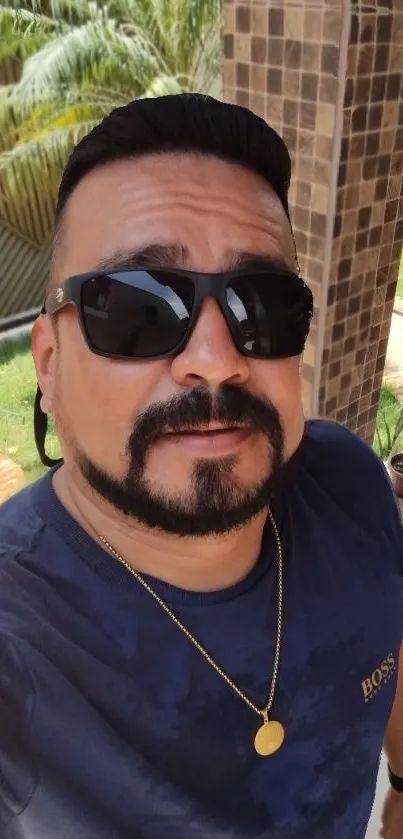 Man with sunglasses and blue shirt posing outdoors.