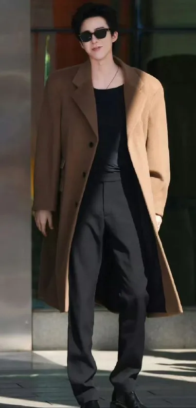 A stylish man in a brown coat and sunglasses, standing with confidence.