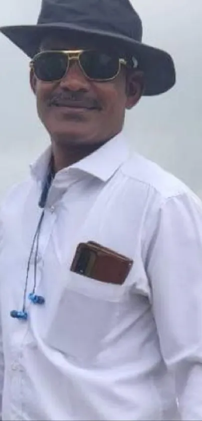 Man with sunglasses and hat in white shirt against cloudy backdrop.