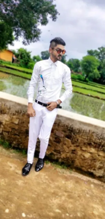 Man in white outfit stands by a village pond.