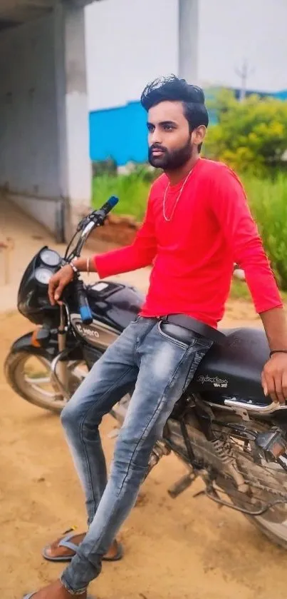 Man in red shirt leaning on a black motorcycle.