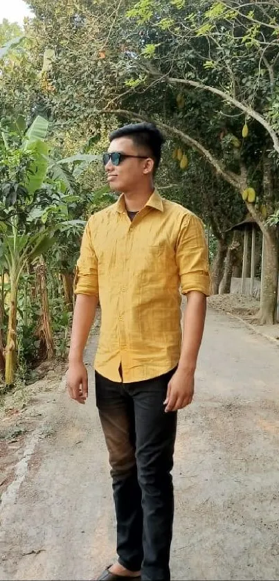 Man in yellow shirt walking on tree-lined path.