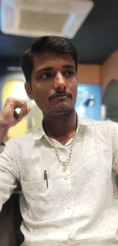 Portrait of a stylish man in a white shirt against a blurred background.