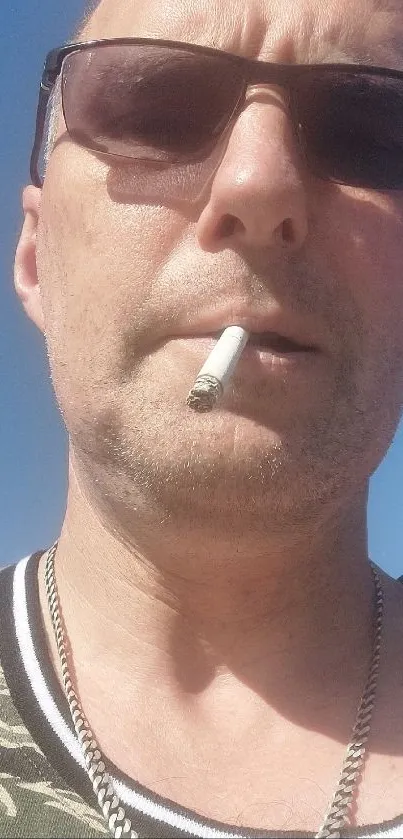 Man with sunglasses and cigarette against blue sky.