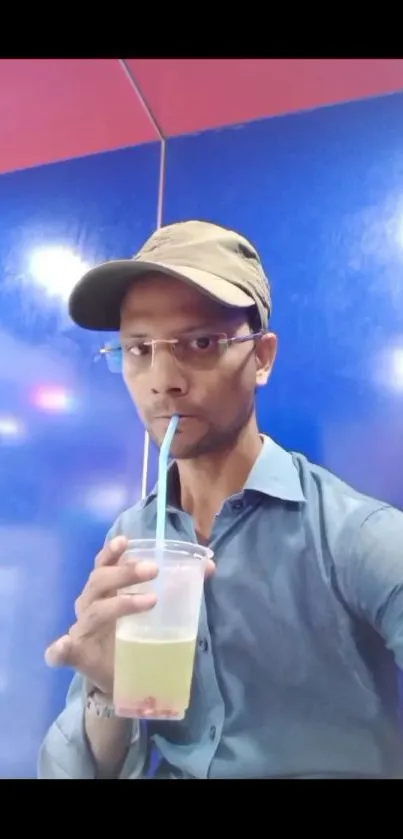 Man sipping a drink against a vibrant blue background.