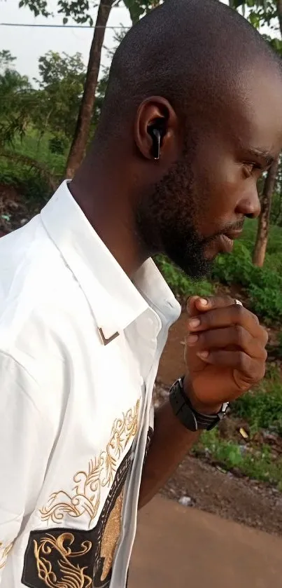 Man with earbuds in park, wearing a designer shirt.