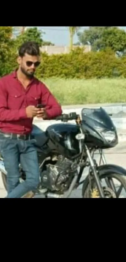 Man in red shirt leaning on motorcycle in outdoor setting.