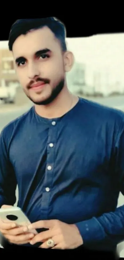 Man in dark blue shirt holding smartphone in urban setting.