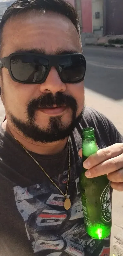 A man wearing sunglasses holding a green bottle in an urban setting.