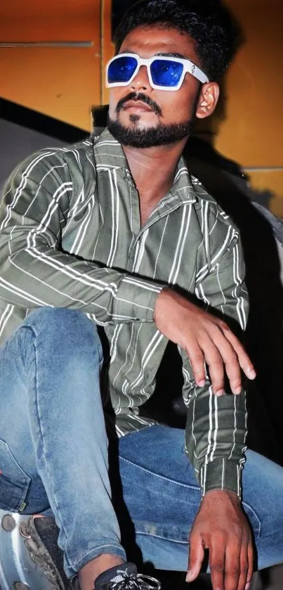 Stylish man in sunglasses and striped shirt, sitting casually.