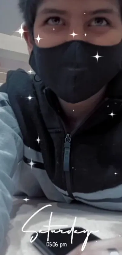 Masked person with hoodie and starry effects on a wallpaper.