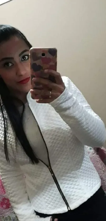 Woman in white jacket takes selfie in mirror with phone.