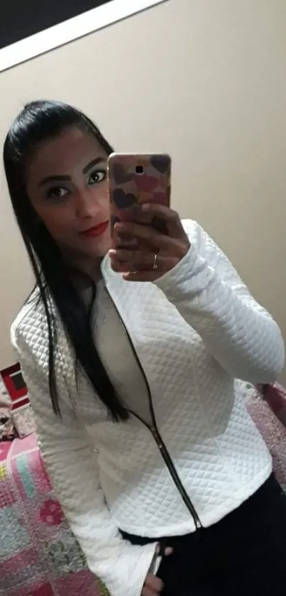 Mirror selfie of a woman in a white jacket holding a phone.