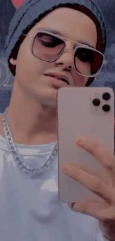 Young man takes a mirror selfie with a phone, wearing casual attire and sunglasses.