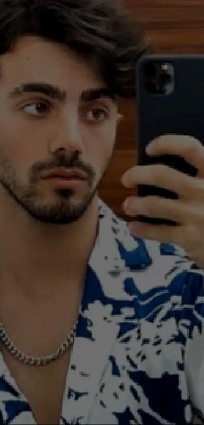 Stylish mirror selfie with man in patterned shirt holding smartphone.