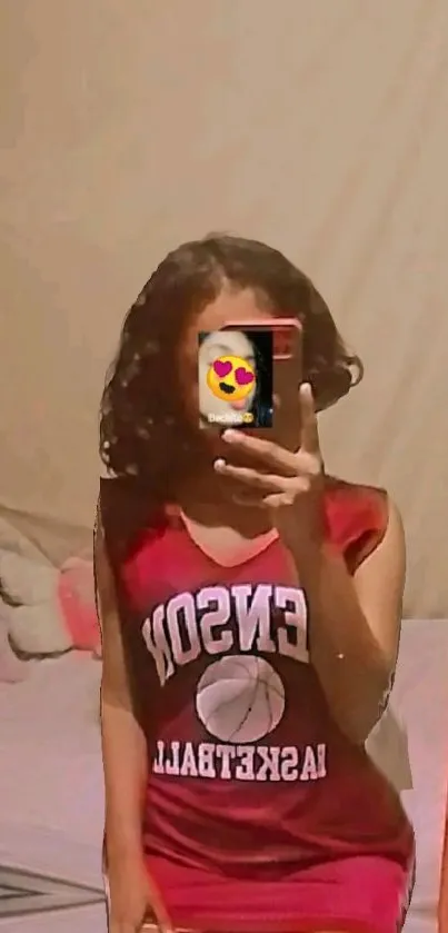 Mirror selfie with trendy red jersey and heart emoji phone cover.