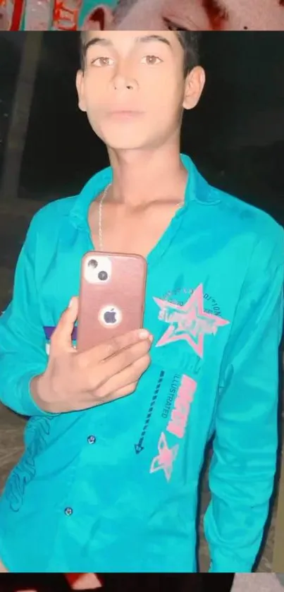 Mirror selfie in teal shirt holding a smartphone.