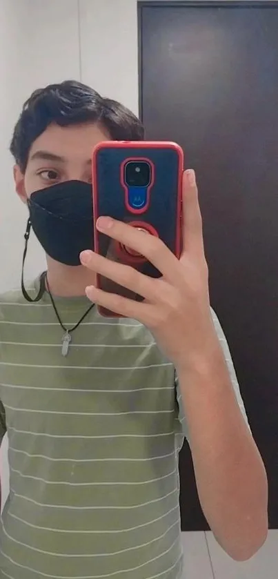 Person taking a mirror selfie with a phone wearing a mask and striped shirt.