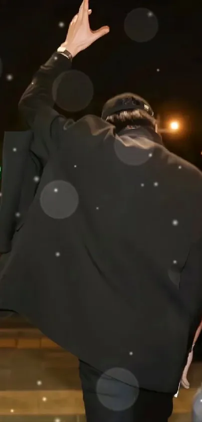 Back view of person raising hand in stylish dark coat at night.