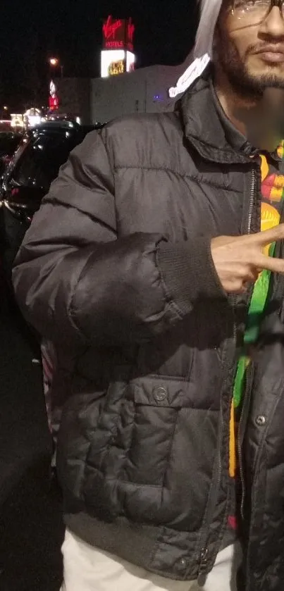 Person in a black puffer jacket at night in urban setting with peace sign.