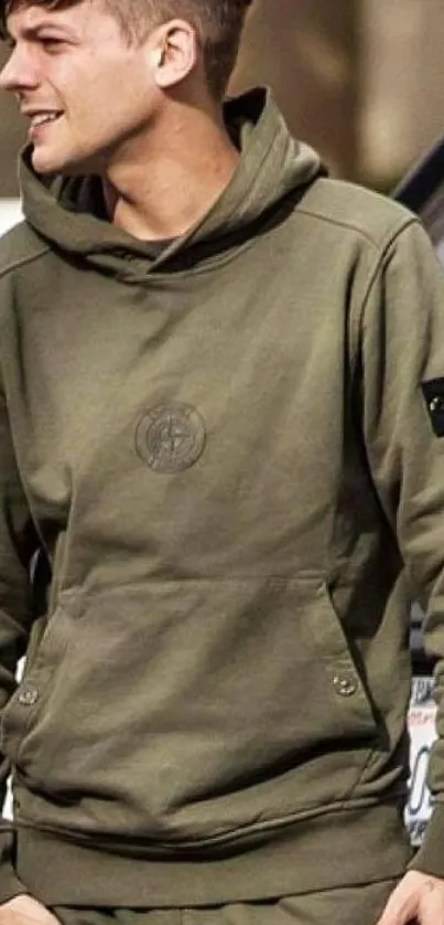 Person wearing olive green hoodie with emblem, casual fashion.