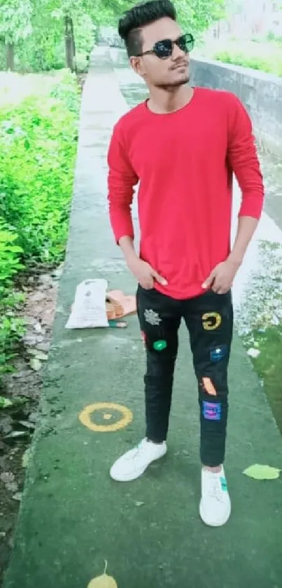 Man in red shirt and jeans, standing outdoors with green background.