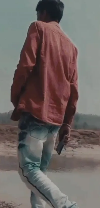 Stylish man in red shirt and jeans by a serene outdoor landscape.