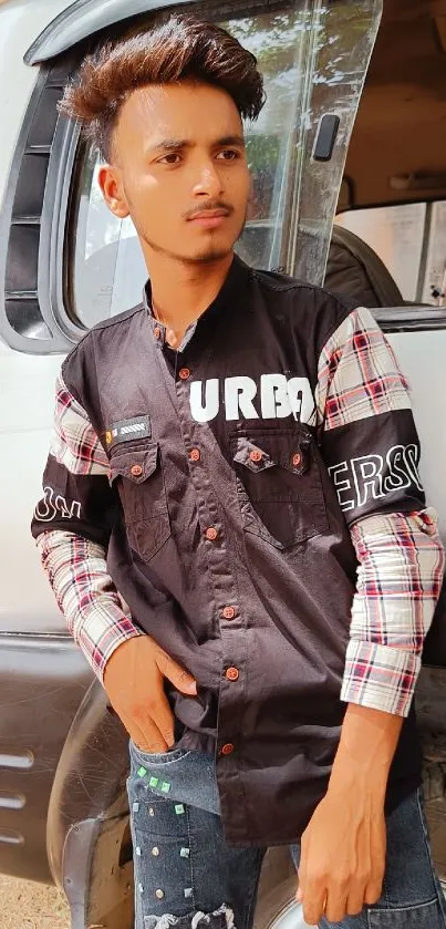 Stylish man posing outdoors with vehicle backdrop.