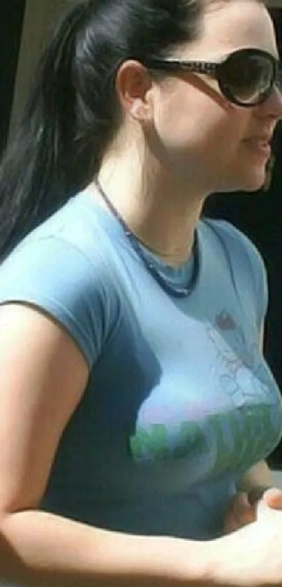 Woman in sunglasses and blue shirt outdoors.