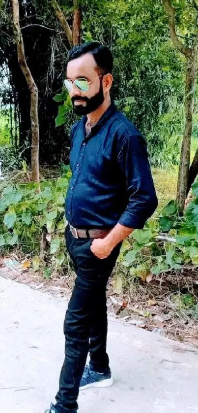 Man in stylish attire posing outdoors near green foliage.