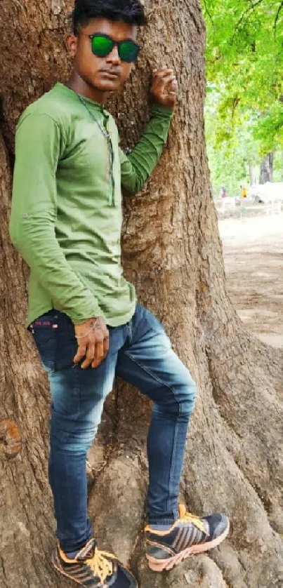 Young man in green shirt leans against large tree.