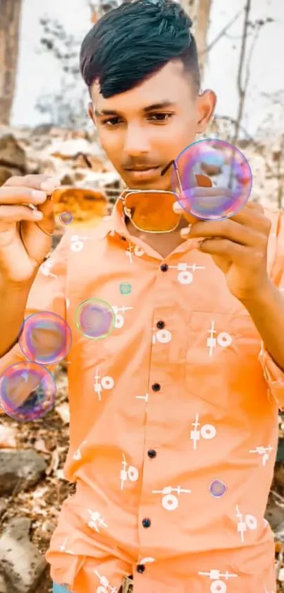 Young man outdoors in stylish orange shirt, holding glasses.