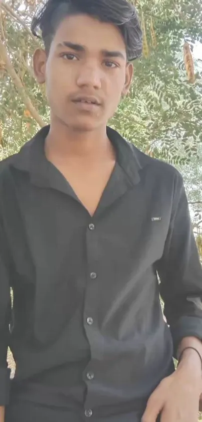 Young man in black shirt outdoors, vibrant nature background.