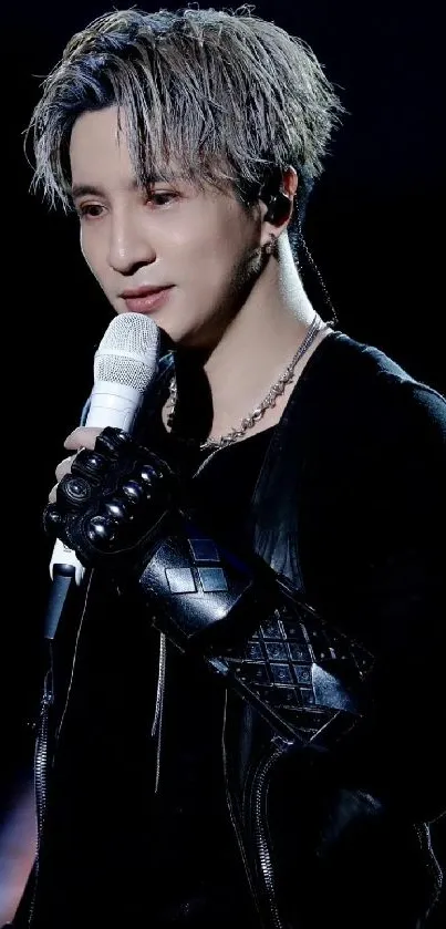 Stylish performer in black attire holding a microphone on stage.