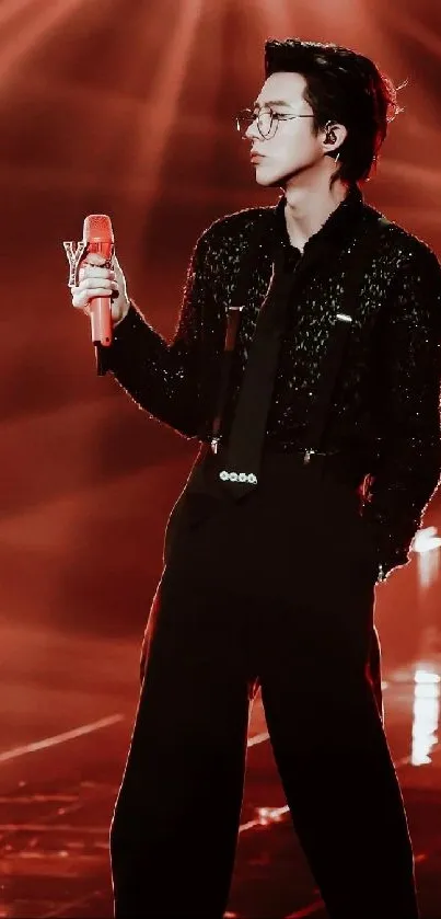 Stylish performer in elegant black outfit under red stage lights.