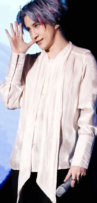 Stylish performer in pale pink shirt holding a microphone on stage.