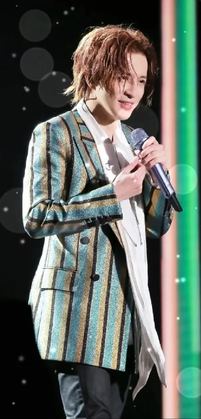 Performer wearing a stylish striped blazer on stage with dark teal background.