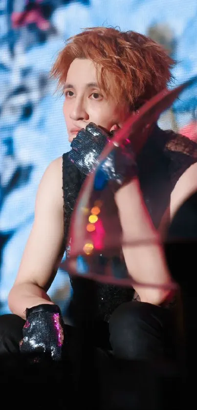 Performer in black with gloves on stage, deep in thought.