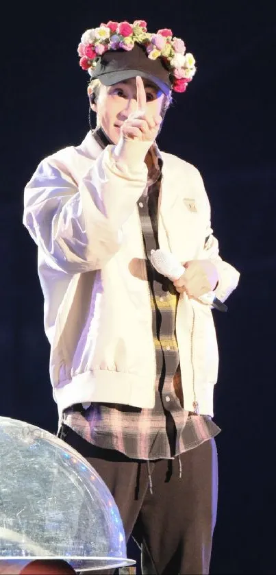 Performer on stage wearing a rose-adorned hat under bright lights.