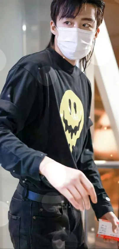 Person in black with yellow smiley face design, wearing a mask.