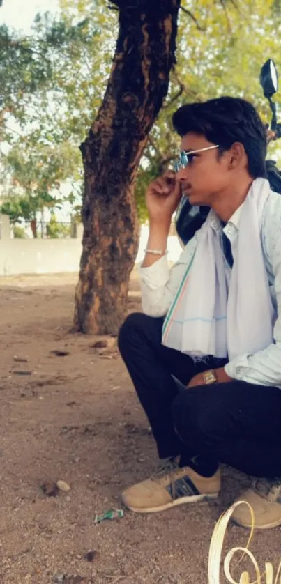 Person sitting under a tree wearing sunglasses with a trendy style.