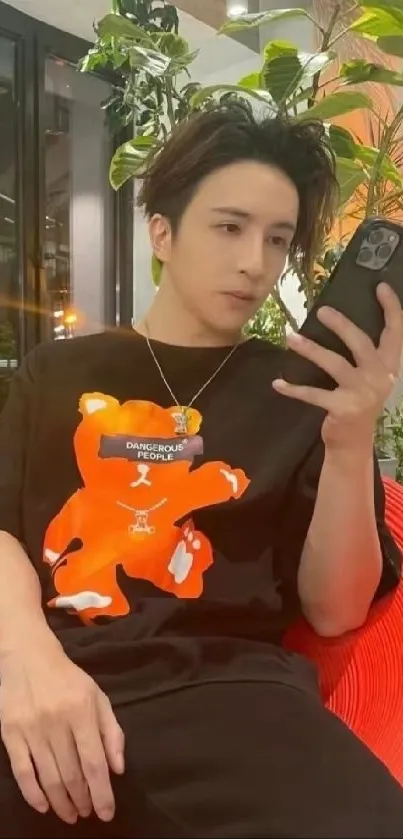 Stylish person holding a phone with lush plants and orange accents.