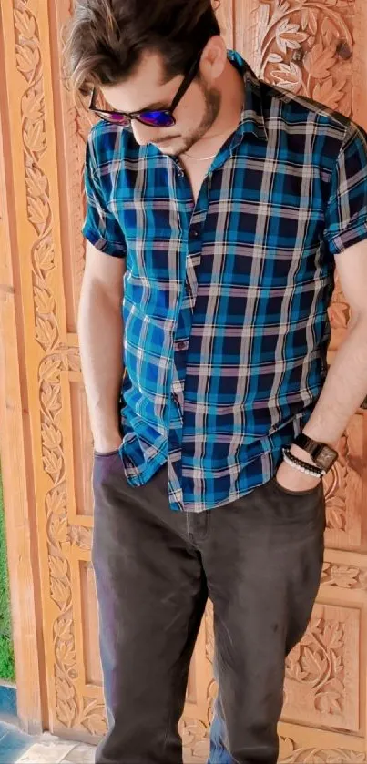 Man wearing plaid shirt in front of ornate wooden door.