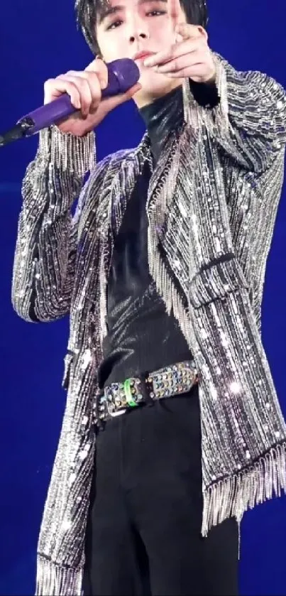 Pop star in a silver jacket sings on stage with purple microphone.