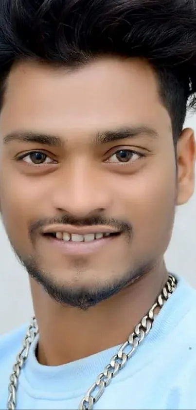 Portrait of a smiling person wearing a light blue shirt and chain.